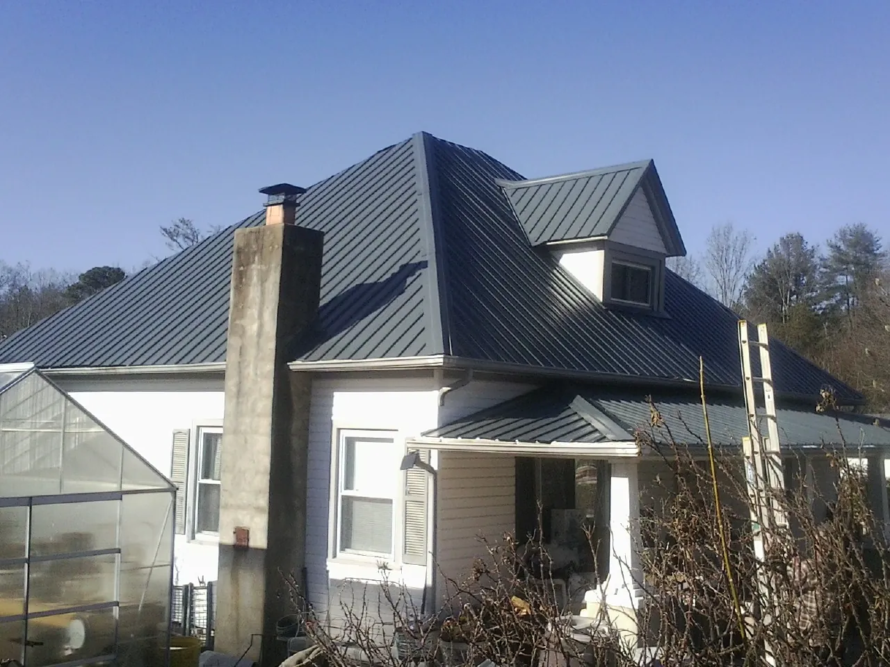 Dark blue standing seam metal roof on a white farmhouse with dormer — Slate & Tile Roof Repair by Roofing Brothers in Acushnet