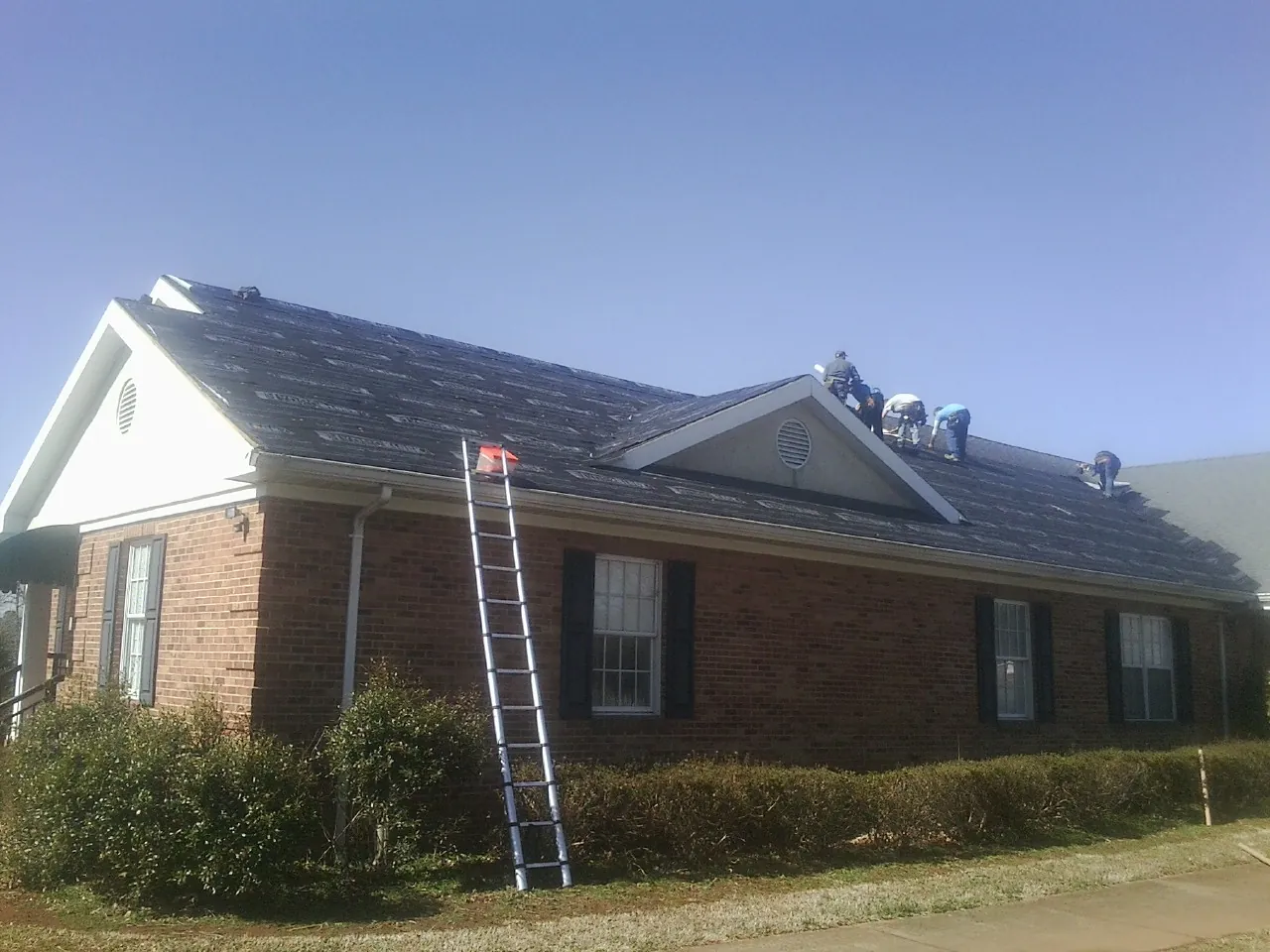 Crew tearing shingles off a brick ranch roof with a ladder set — Emergency Roof Repair work by our crew in Acushnet