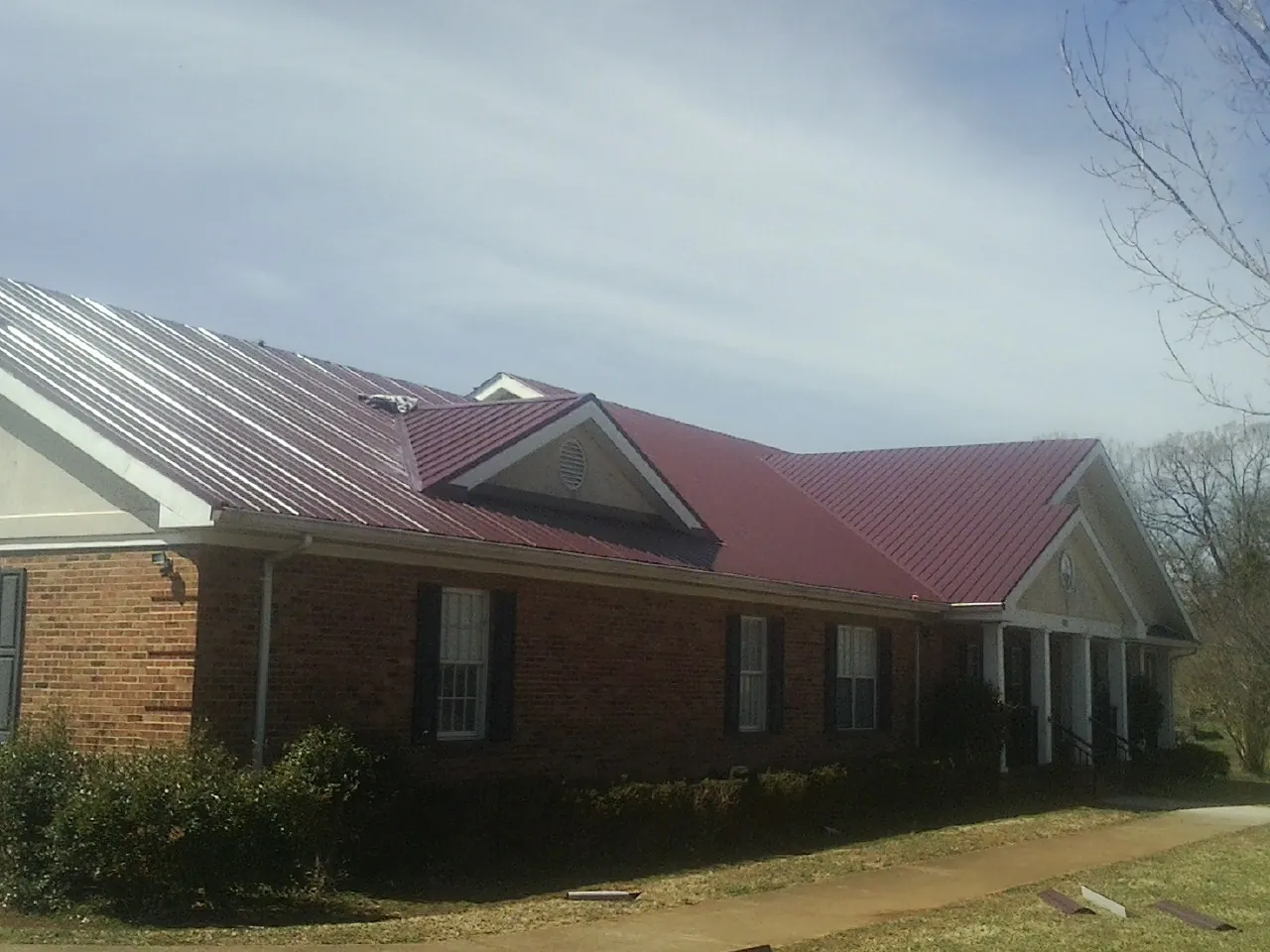 Red metal roof with gabled entries on a long brick building, from a Hail Damage Roof Repair job in Acushnet