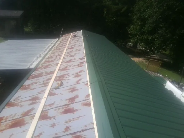 Old rusted panels beside newly installed green metal roofing in Acushnet