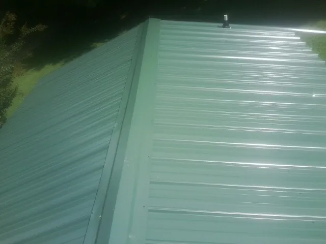 New green metal panels meeting at the ridge of a roof — Flat Roof Repair work by our crew in Acushnet