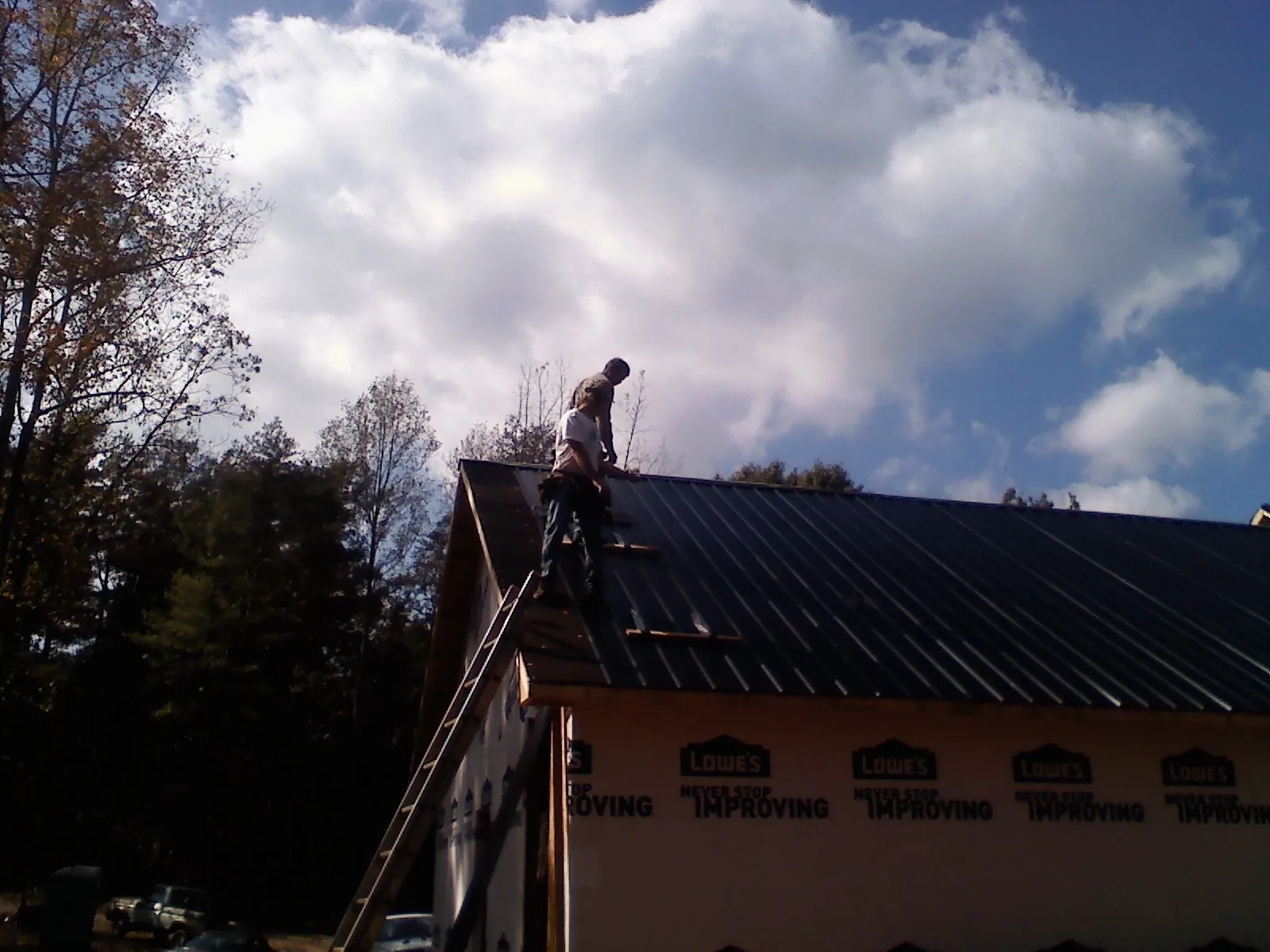 Roofer fastening dark metal panels high against a cloudy sky, from a Roof Inspection job in Acushnet